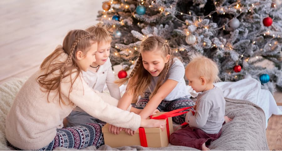 Children opening a present in the family room next to a Christmas tree.